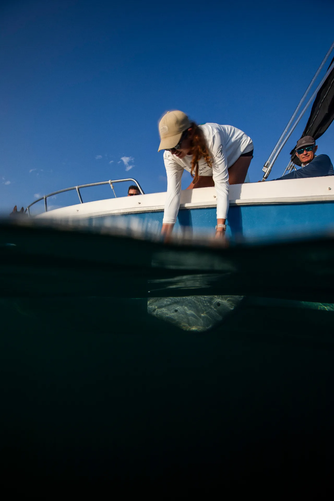 Marine biologist reaching into the sea from a research boat, with a reef visible underwater