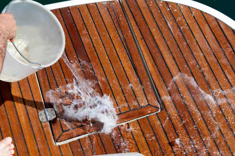 Man pouring fresh water on a wooden boat dec