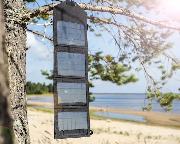 a black portable foldable solar panel with a power bank hanging from a tree