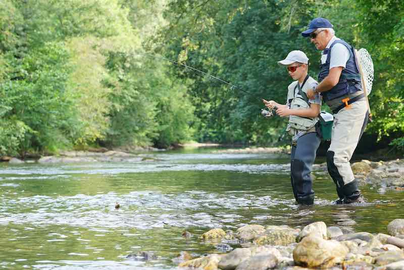 Grandfather and grandson fishing for trout in a mountain river