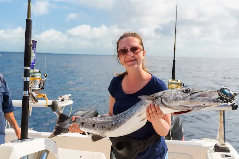 Woman holding big fish on a fishing boat on a sunny day. Onboard personal hygiene